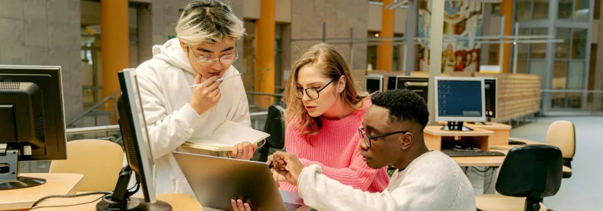 Three higher education students working together around a computer.