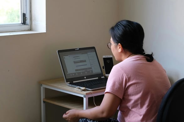 Student with glasses in salmon-colored shirt starting at computer with phone nearby