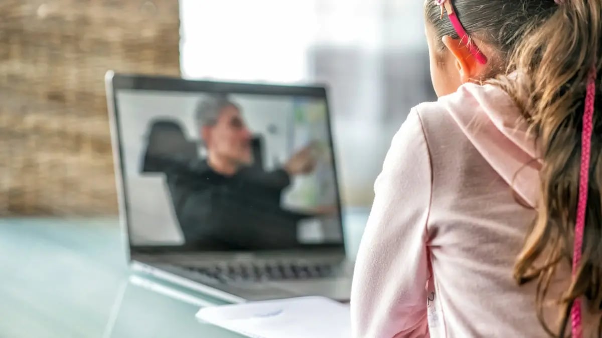 Young female student on computer laptop listening to male teacher and taking notes.