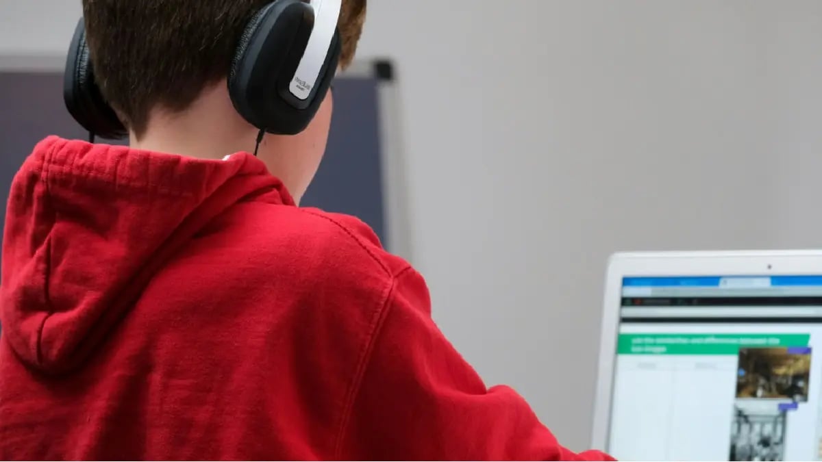 Young male student with headphones and a red sweatshirt doing an assignment on the computer.