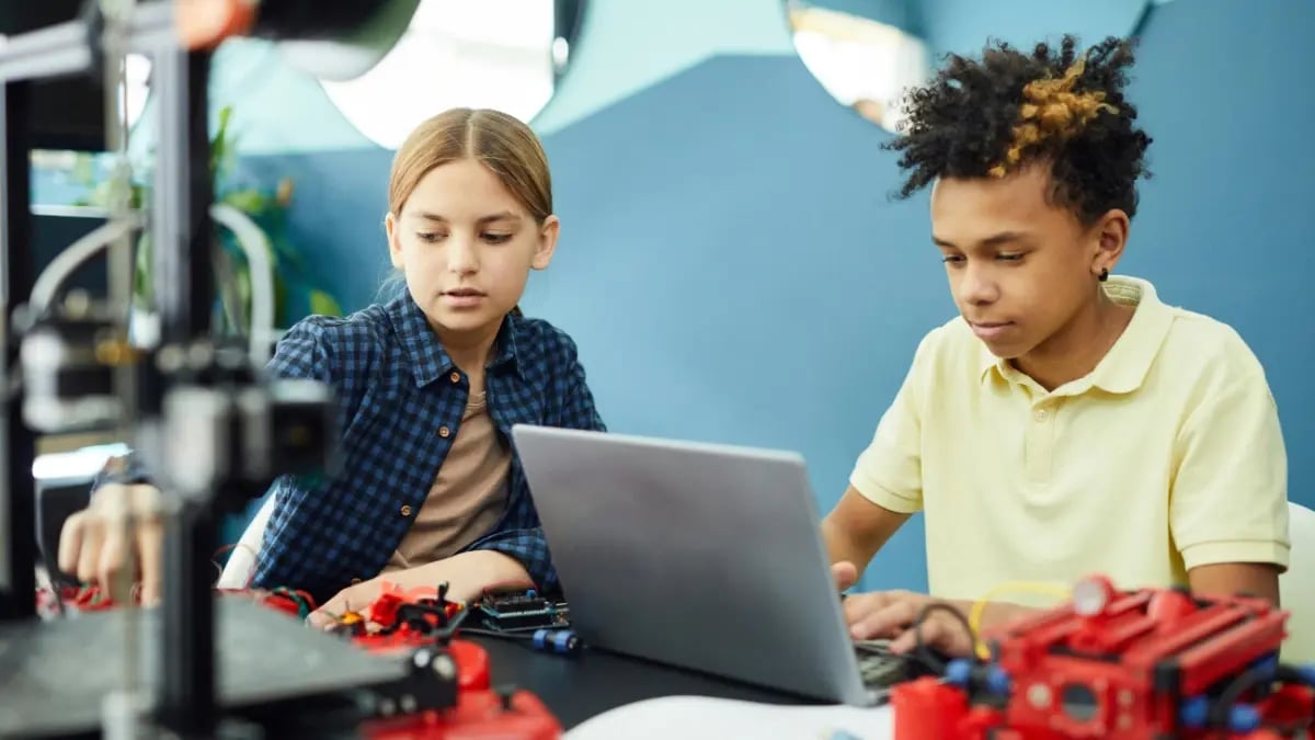 Two students sitting next to each other in science class: One interacting with objects and one typing on the laptop.