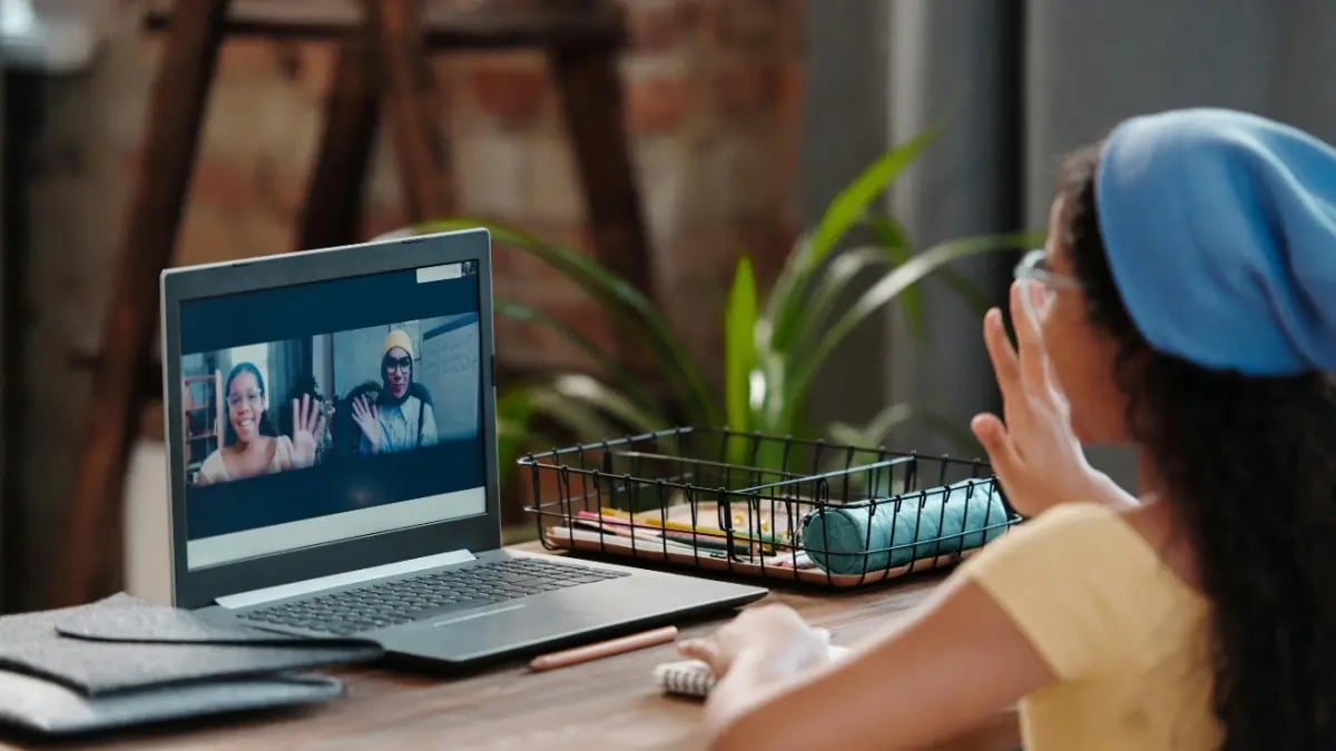 Female student waving to two classmates on computer.