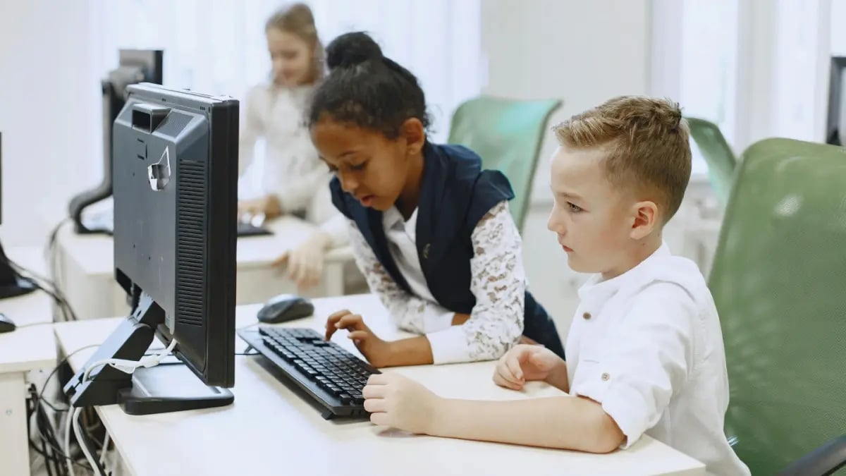 Two young students sitting together typing at a computer.