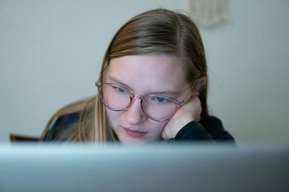 Blonde student with glasses leaning into her hand on her face staring at the computer