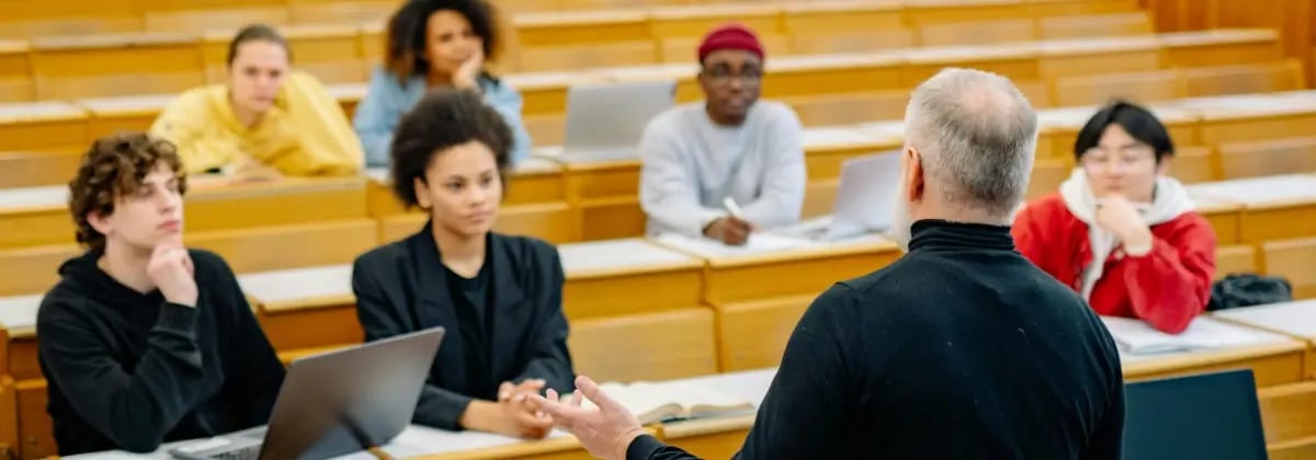 A group of higher education students listening to an instructor teach in a lecture hall.