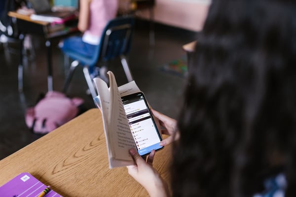 Student sneakily looking at phone in a book to disguise phone usage.