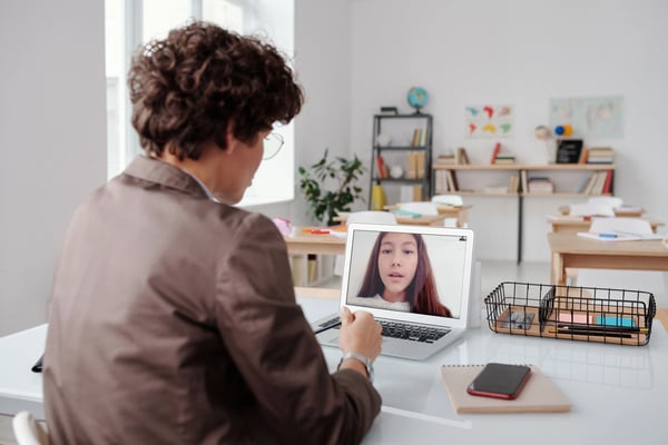 Young male learner on a video call with a female in a home classroom environment.