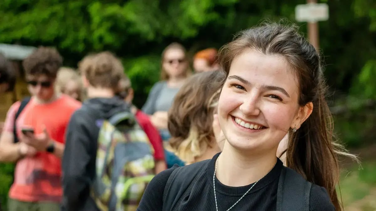 High school-aged student with backpack smiling near group of other students
