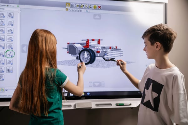 One male and one female K-8 student working on a project together in front of a projector.