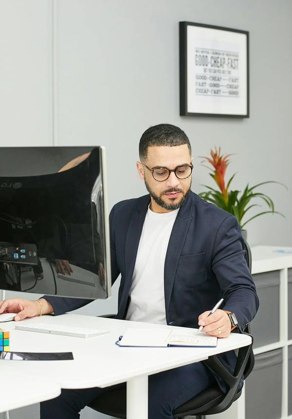 Gentleman in glasses and casual black suit writing notes at the computer.