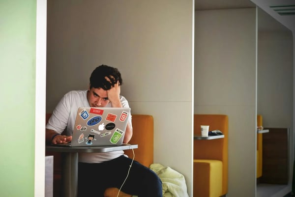Male college student on a plugged-in laptop with hand on his head in focus mode.